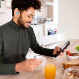 Young man with hearing aids checking his phone over breakfast.